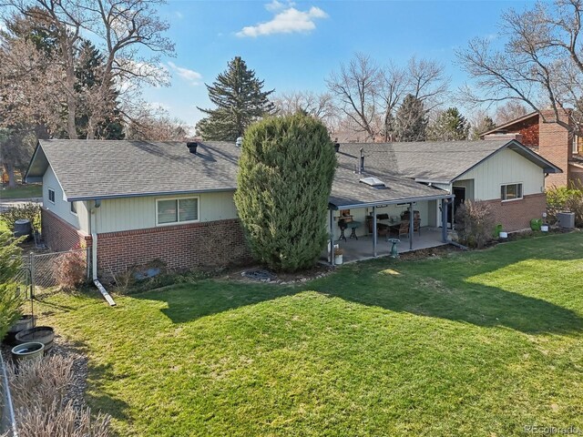 rear view of house with a yard, a patio, fence, brick siding, and a shingled roof