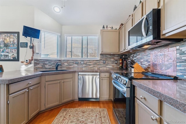 kitchen featuring vaulted ceiling, appliances with stainless steel finishes, sink, backsplash, and light hardwood / wood-style flooring