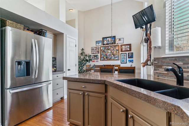 kitchen featuring stainless steel refrigerator with ice dispenser, sink, hanging light fixtures, light hardwood / wood-style floors, and decorative backsplash