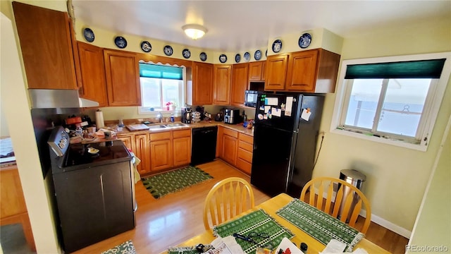 kitchen with black appliances, sink, extractor fan, and light hardwood / wood-style flooring