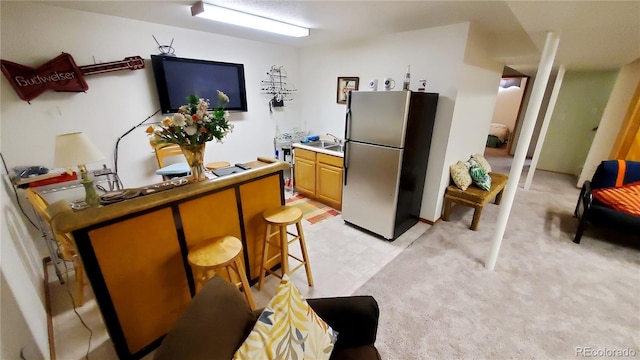 kitchen with stainless steel refrigerator, a breakfast bar, light colored carpet, and sink