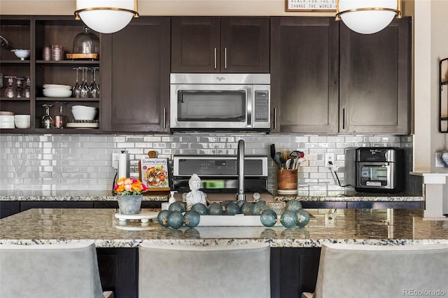 14110 Pastel Ln, Parker, CO 80134 - kitchen with stainless steel microwave, dark brown cabinetry, stove, backsplash, and light stone countertops