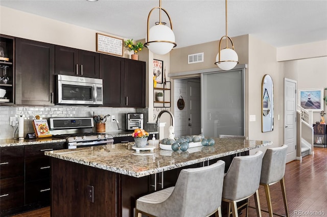 14110 Pastel Ln, Parker, CO 80134 - kitchen with stainless steel appliances, decorative backsplash, dark wood-style flooring, a kitchen breakfast bar, and hanging light fixtures