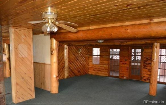 unfurnished living room featuring dark carpet, rustic walls, wood ceiling, ceiling fan, and wood walls