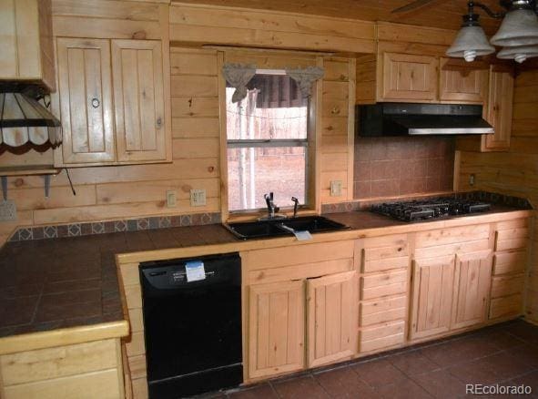 kitchen featuring gas cooktop, wooden walls, sink, black dishwasher, and tile counters