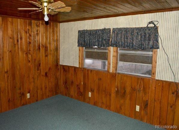 unfurnished room featuring carpet flooring, ceiling fan, wooden ceiling, and wood walls