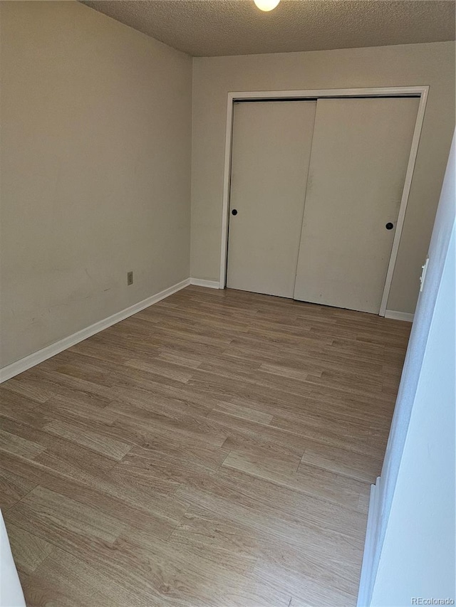 unfurnished bedroom featuring a closet, a textured ceiling, and light wood-type flooring