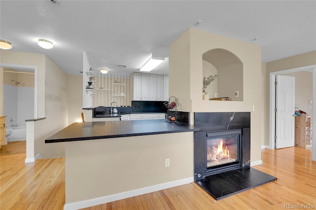 kitchen with white cabinetry, sink, backsplash, kitchen peninsula, and light hardwood / wood-style flooring