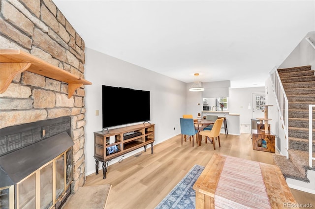 living area featuring stairs, a stone fireplace, and wood finished floors