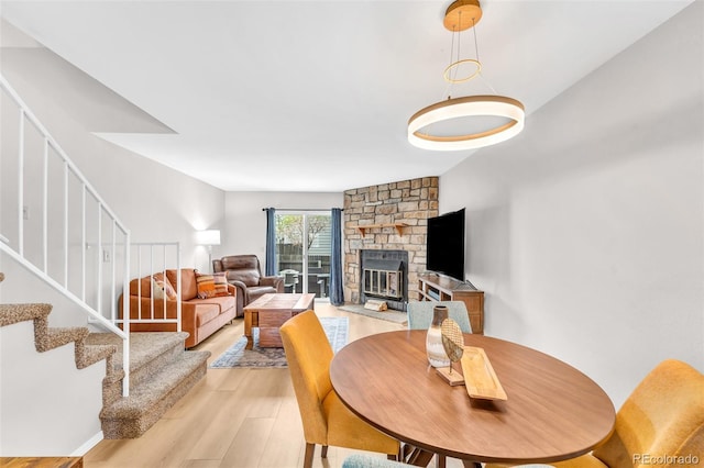 dining area featuring light wood finished floors, a stone fireplace, and stairs