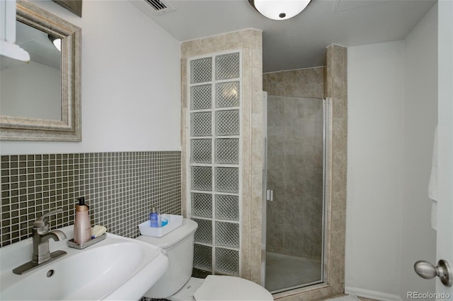 bathroom with toilet, a shower with shower door, sink, and tile walls