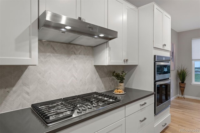 kitchen with white cabinets, stainless steel appliances, light wood-type flooring, and tasteful backsplash