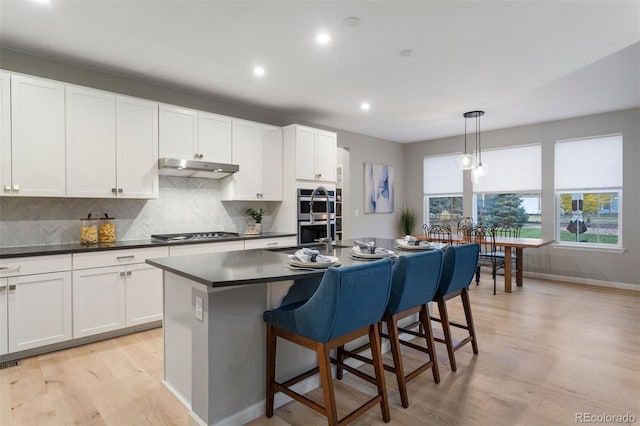 kitchen with decorative light fixtures, a kitchen island with sink, white cabinetry, and appliances with stainless steel finishes