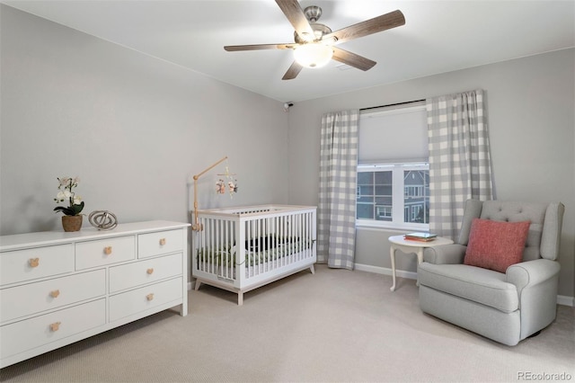 bedroom with light colored carpet, ceiling fan, and a nursery area