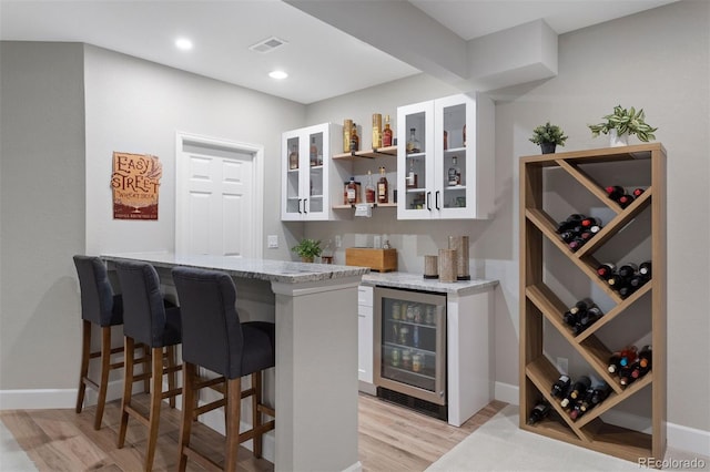 bar with light stone countertops, white cabinets, light hardwood / wood-style flooring, and wine cooler