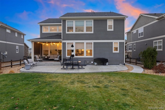 back house at dusk with a patio area and a lawn