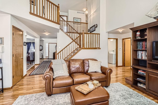 living room with a towering ceiling, stairway, washer / dryer, visible vents, and light wood finished floors