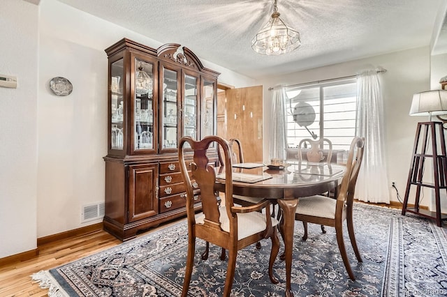 dining area with light wood-style floors, a notable chandelier, visible vents, and a textured ceiling