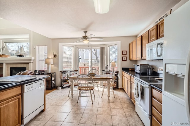 kitchen with ceiling fan, light tile patterned floors, white appliances, brown cabinetry, and dark countertops