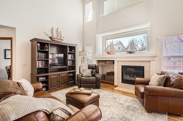 living room with a healthy amount of sunlight, wood finished floors, a fireplace, and a towering ceiling