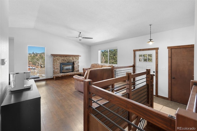 living room featuring lofted ceiling, a stone fireplace, hardwood / wood-style flooring, ceiling fan, and a textured ceiling