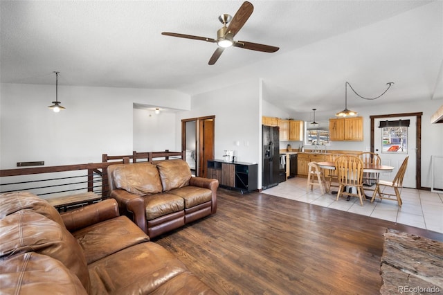 living room featuring a textured ceiling, ceiling fan, vaulted ceiling, and light wood-type flooring