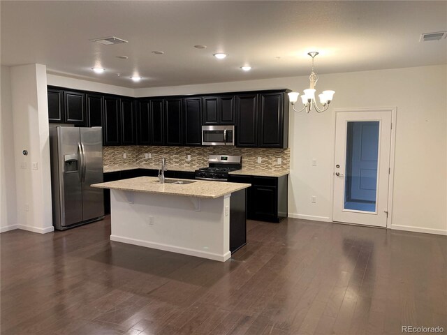 kitchen with light stone counters, stainless steel appliances, sink, an island with sink, and dark wood-type flooring