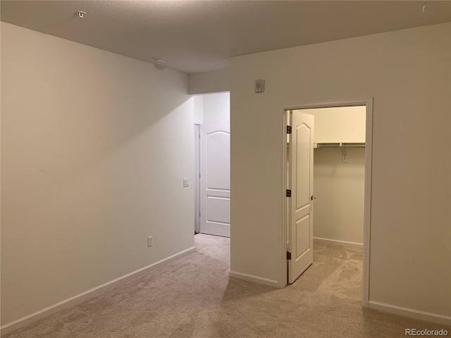 unfurnished bedroom featuring a walk in closet, light colored carpet, and a closet