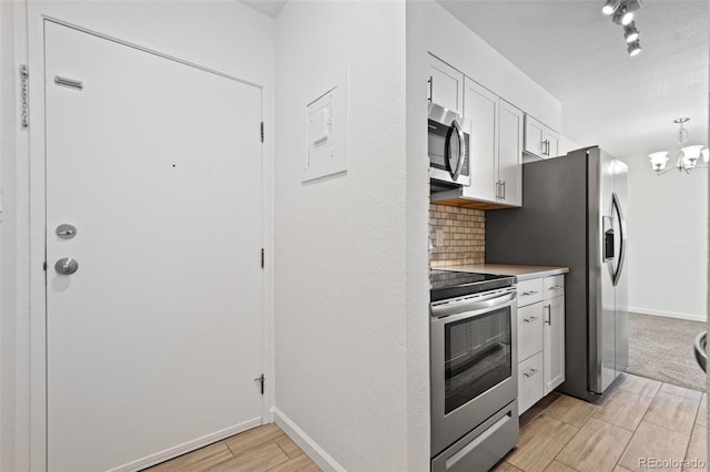 kitchen featuring stainless steel appliances, a notable chandelier, white cabinets, and tasteful backsplash