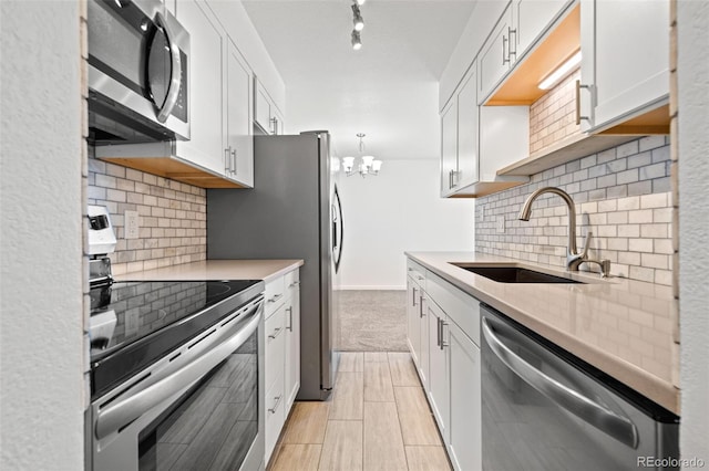 kitchen with stainless steel appliances, sink, decorative light fixtures, white cabinets, and a notable chandelier