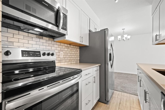 kitchen featuring stainless steel appliances, an inviting chandelier, pendant lighting, and white cabinetry