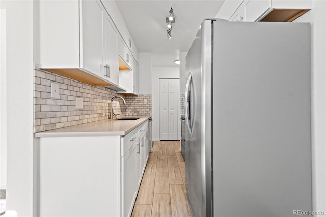 kitchen with sink, white cabinets, light hardwood / wood-style flooring, track lighting, and stainless steel refrigerator