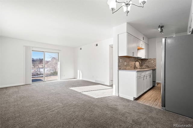 kitchen featuring sink, white cabinetry, decorative backsplash, stainless steel fridge, and a chandelier