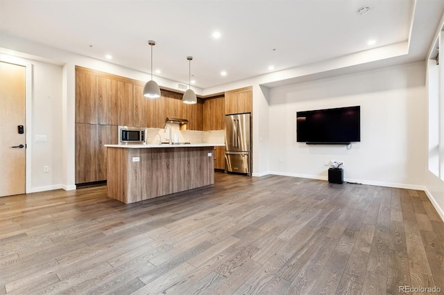 kitchen with appliances with stainless steel finishes, an island with sink, hardwood / wood-style flooring, and pendant lighting