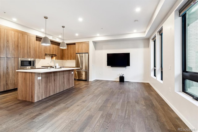 kitchen featuring decorative light fixtures, dark wood-type flooring, stainless steel appliances, sink, and a kitchen island with sink