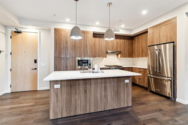 kitchen featuring appliances with stainless steel finishes, decorative light fixtures, dark wood-type flooring, sink, and a center island with sink