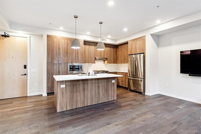 kitchen with dark wood-type flooring, hanging light fixtures, stainless steel appliances, and an island with sink