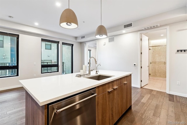 kitchen featuring sink, hanging light fixtures, a kitchen island with sink, stainless steel dishwasher, and light hardwood / wood-style flooring