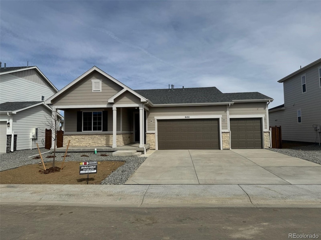 craftsman house with stone siding, an attached garage, concrete driveway, and roof with shingles