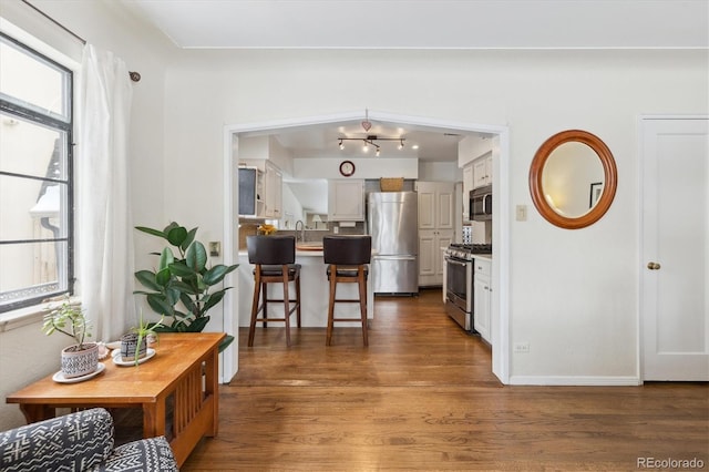 kitchen with white cabinets, appliances with stainless steel finishes, a kitchen bar, dark wood-type flooring, and sink