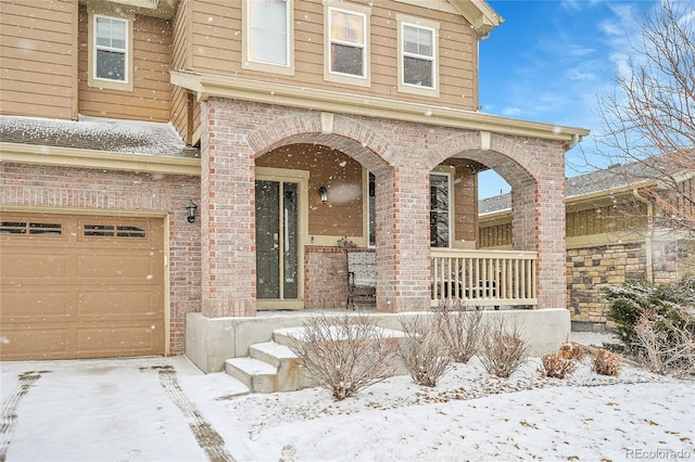 snow covered property entrance featuring a garage and a porch