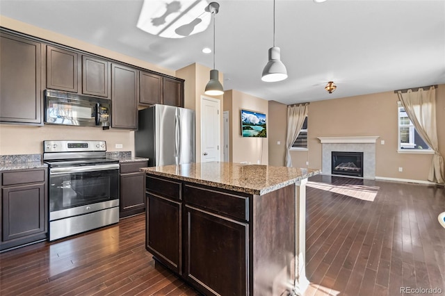 kitchen featuring appliances with stainless steel finishes, dark hardwood / wood-style floors, hanging light fixtures, dark brown cabinetry, and light stone countertops