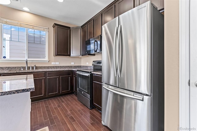 kitchen featuring sink, dark brown cabinets, dark hardwood / wood-style flooring, stainless steel appliances, and light stone countertops