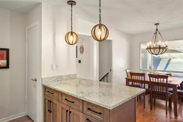 kitchen featuring dark wood-type flooring, decorative light fixtures, kitchen peninsula, and light stone counters