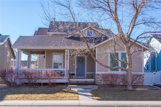 view of front of house with covered porch, a shingled roof, and stone siding