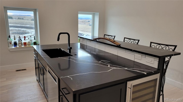 kitchen with light hardwood / wood-style floors, a kitchen island with sink, sink, and wine cooler