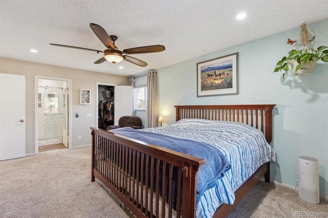 bedroom featuring ensuite bath, a walk in closet, light colored carpet, ceiling fan, and a textured ceiling