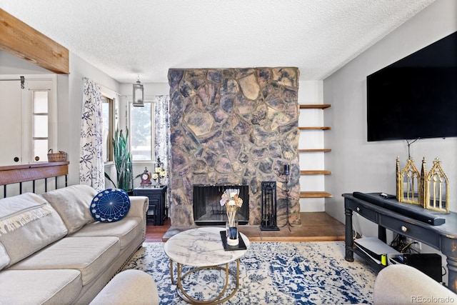 living room featuring a textured ceiling, a stone fireplace, and wood finished floors