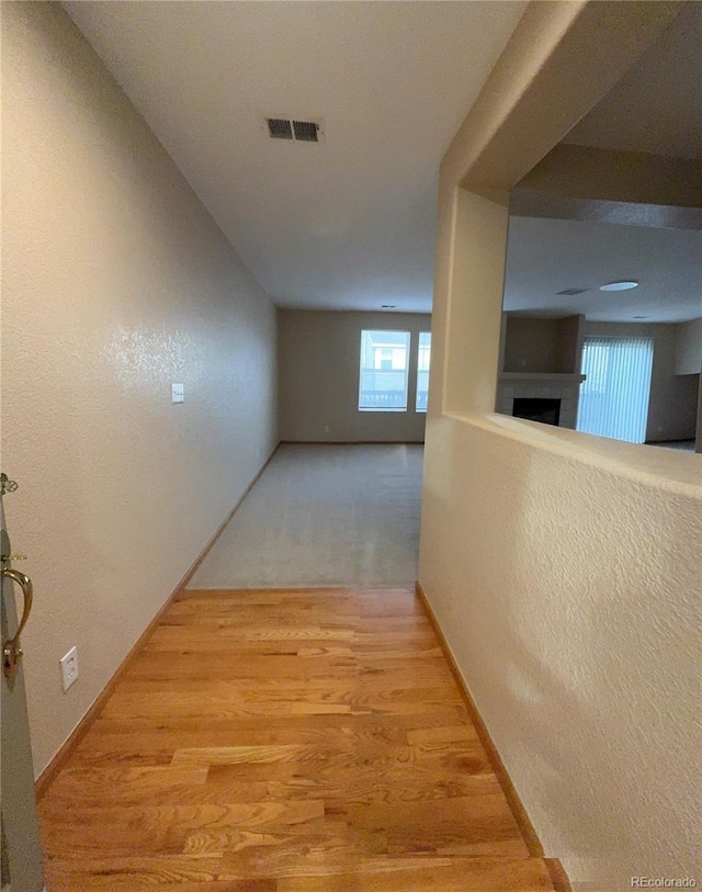 hallway with a textured wall, baseboards, visible vents, and wood finished floors