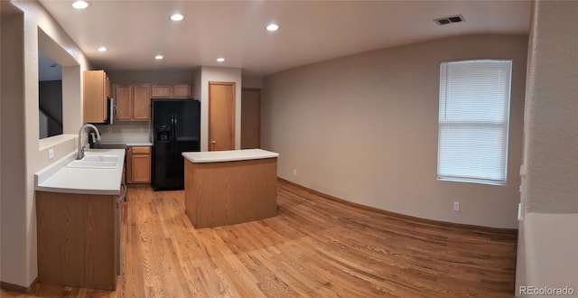 kitchen featuring black refrigerator with ice dispenser, a center island, visible vents, a sink, and light wood-type flooring